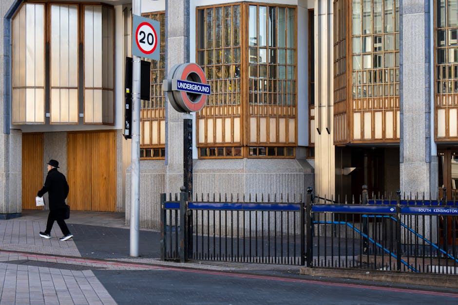 Photograph of a row of red-brick residential buildings along a quiet street in South Kensington, featuring multiple stories with large sash windows and decorative iron balconies, under a clear blue sk