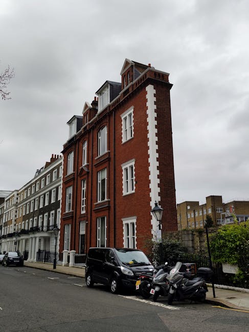 Street view of a row of commercial storefronts in South Kensington, London, with large glass display windows showcasing flowers and plants. The buildings have elegant white and pastel-colored facades,